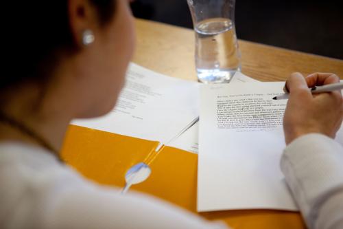 View over a student's shoulder as she writes on a piece of paper at a desk