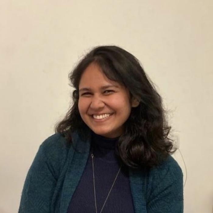 Photograph of Ananya, who has medium-length black hair, wearing a green sweater and black turtleneck.
